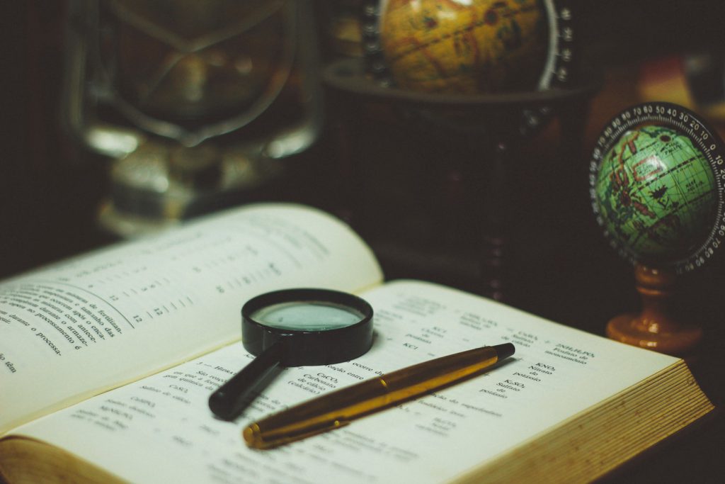 decorative image: open book with magnifying glass and pen