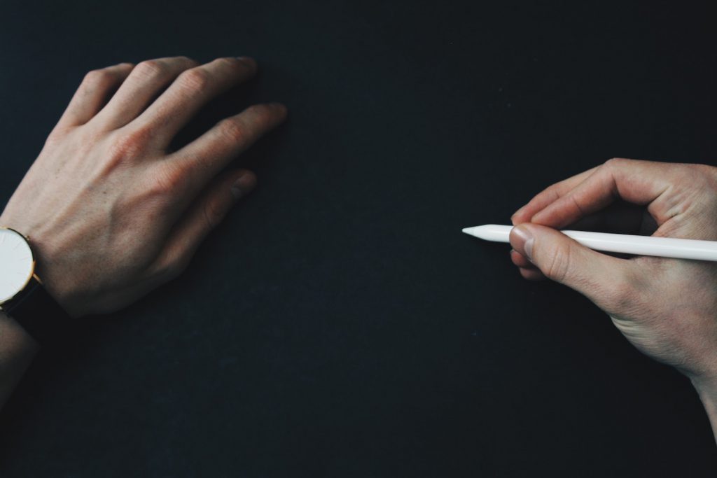 decorative image: hands and pencil on black surface